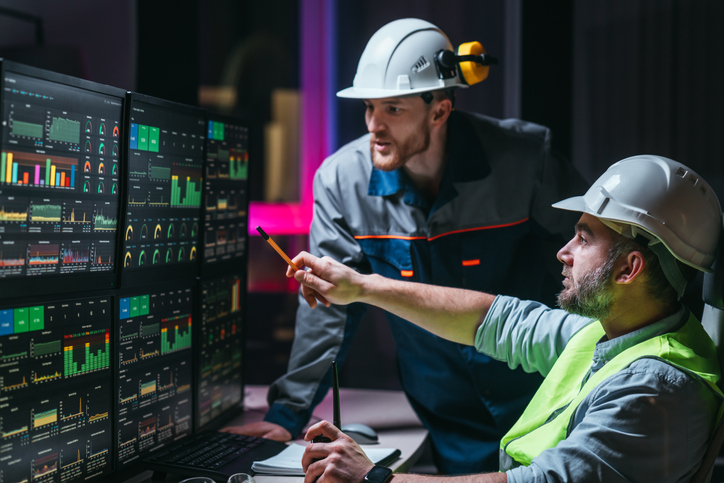 Head engineer and worker following factory production line uses screens with Industry 4.0 software. Couple of facility operators checking and analyzing process.