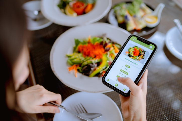 Young woman using mobile app device on smartphone to place a food order in a restaurant.