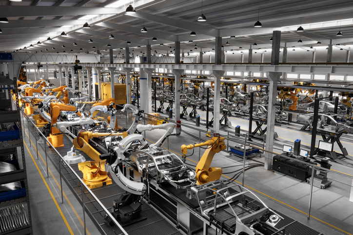 High angle view of cars on production line in factory. Many robottic arms doing welding on car metal body in manufacturing plant.